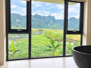 A room with a large window offering a view of a lush landscape with mountains and a river. - Hotel LaVue Tam Coc (Nam Hoa Lu)