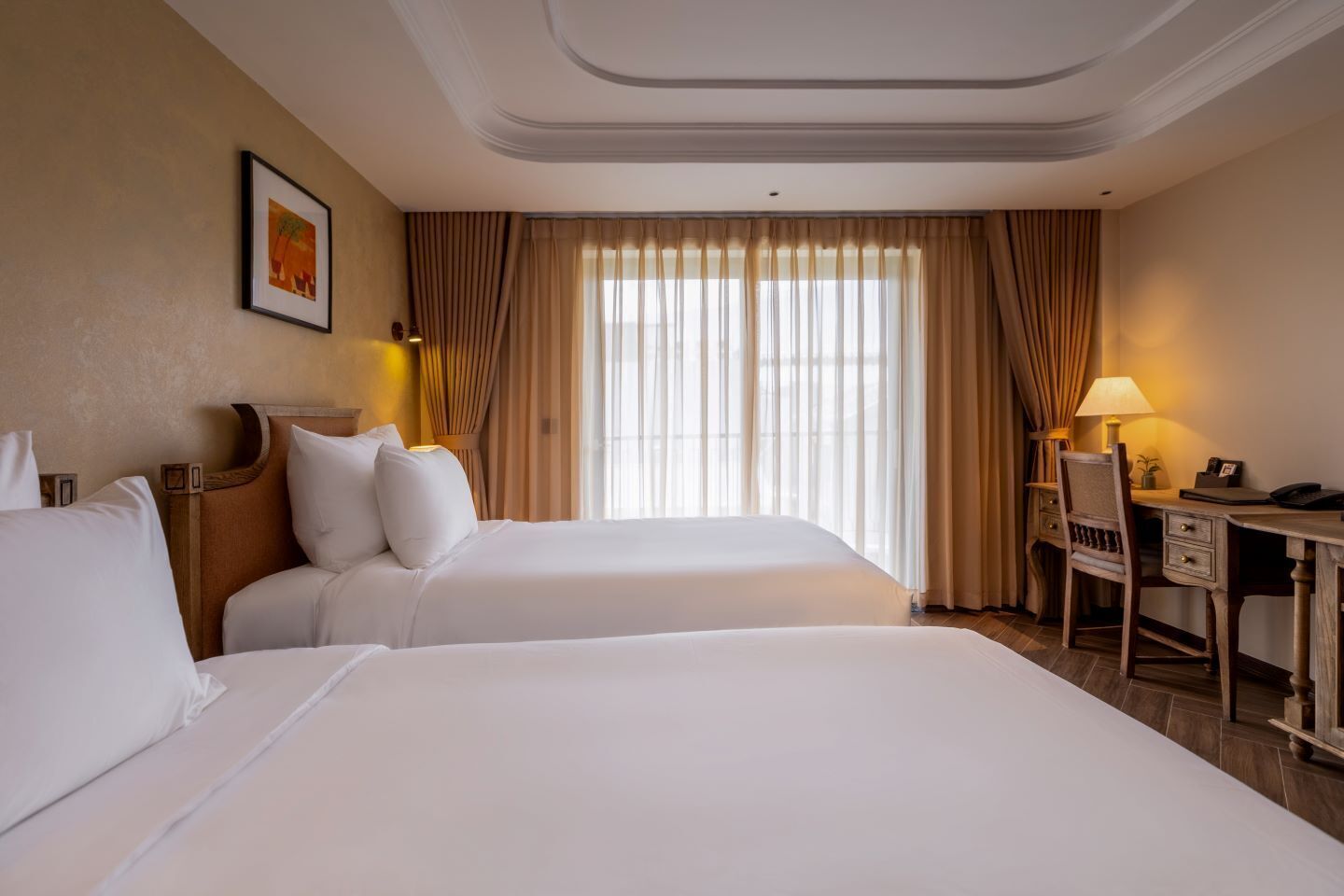 A hotel room with two beds, a desk, a chair, and a large window with curtains.