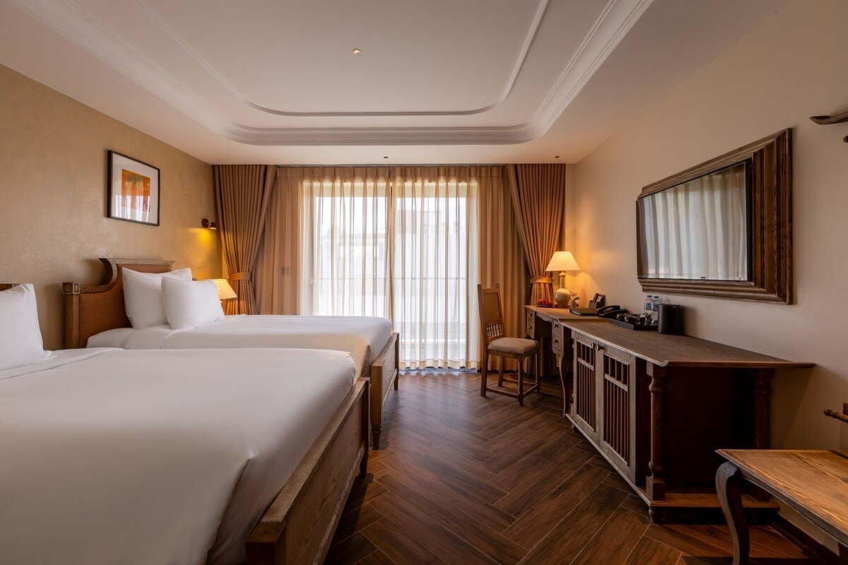 Habitación de hotel con dos camas, un escritorio, una silla, un espejo y un ventanal con cortinas.