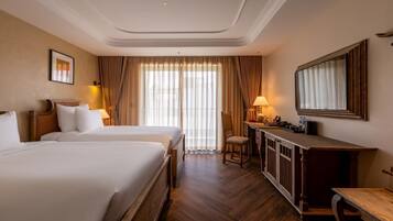 A hotel room with two beds, a desk, a chair, a mirror, and a window with curtains.