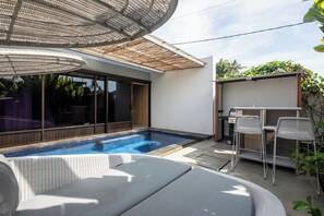 Una piscina con sillones de descanso, una pérgola y una zona de estar cubierta.