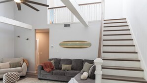 Ein Wohnzimmer mit grauem Sofa, einem gemusterten Teppich, Deckenventilator und einer Treppe.