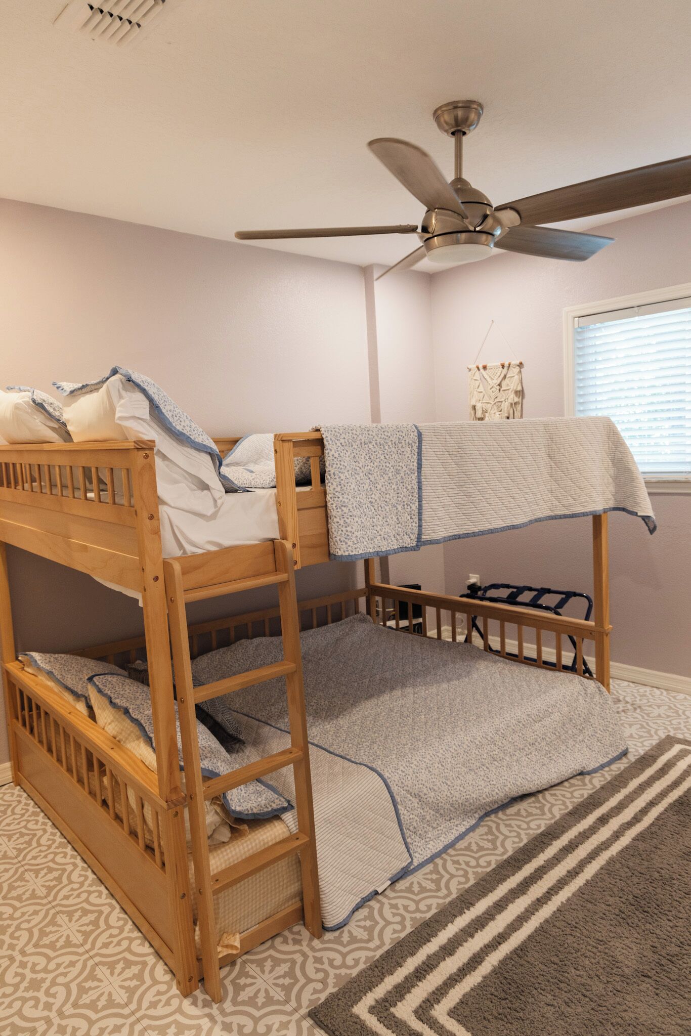A bunk bed room with a ceiling fan, patterned rug, and a window with blinds.