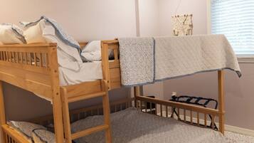 A bunk bed room with a ceiling fan, patterned rug, and a window with blinds.
