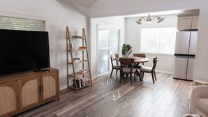 Ein modernes Wohnzimmer mit Flachbildfernseher, einer Holzbücherwand, einem Essbereich mit Stühlen und einer Küche inklusive Kühlschrank.