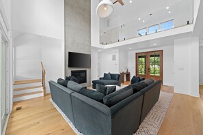 Ein modernes Wohnzimmer mit Ecksofa, Kamin, Fernseher und einer Treppe.