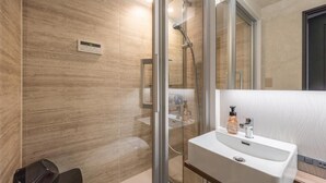 A modern bathroom with a glass-enclosed shower, a white sink with a mirror, and a wooden vanity. - JAPAVISTA Luminous (SHIMANOUCHI, CHUO WARD)
