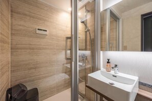 A modern bathroom with a glass-enclosed shower, a white sink with a mirror, and a wooden vanity. - JAPAVISTA Luminous (SHIMANOUCHI, CHUO WARD)