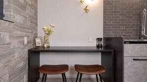 A modern kitchen with a dark countertop, two stools, a vase with flowers, and a wall-mounted light fixture. - JAPAVISTA Luminous (SHIMANOUCHI, CHUO WARD)