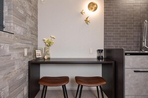 A modern kitchen with a dark countertop, two stools, a vase with flowers, and a wall-mounted light fixture. - JAPAVISTA Luminous (SHIMANOUCHI, CHUO WARD)