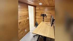 Een kamer met houten lambrisering, een houten tafel, stoelen, een computer en een deur.