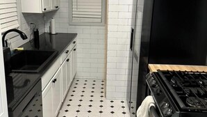 Een keuken met witte kasten, een zwart aanrecht, een spoelbak, een fornuis en een betegelde vloer.