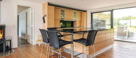A modern kitchen with a central island, black bar stools, and a view to the outdoors.