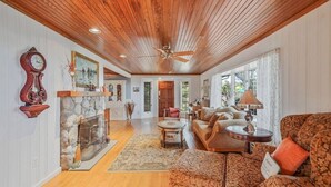 A spacious living room with a fireplace, wooden ceiling, and a large window.