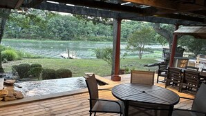 A covered outdoor deck with a view of a lake, a hot tub, and outdoor furniture.