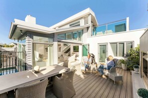 A modern house with a wooden deck, outdoor seating, and a staircase leading to an upper level. - The Lumiere House -Elegance in Mt Maunganui (Mount Maunganui)