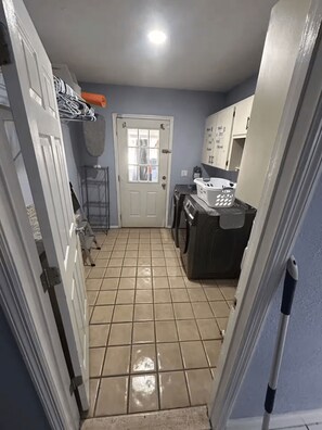 A narrow hallway with a tiled floor, a door with a window, and a laundry area with a washing machine and a drying rack. - Walk to Casino, Fairground, Drive to beaches, King Bed (Tampa)