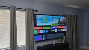 Una sala de estar con un televisor de pantalla plana montado en la pared, un mueble de entretenimiento negro debajo y una alfombra estampada en el suelo.
