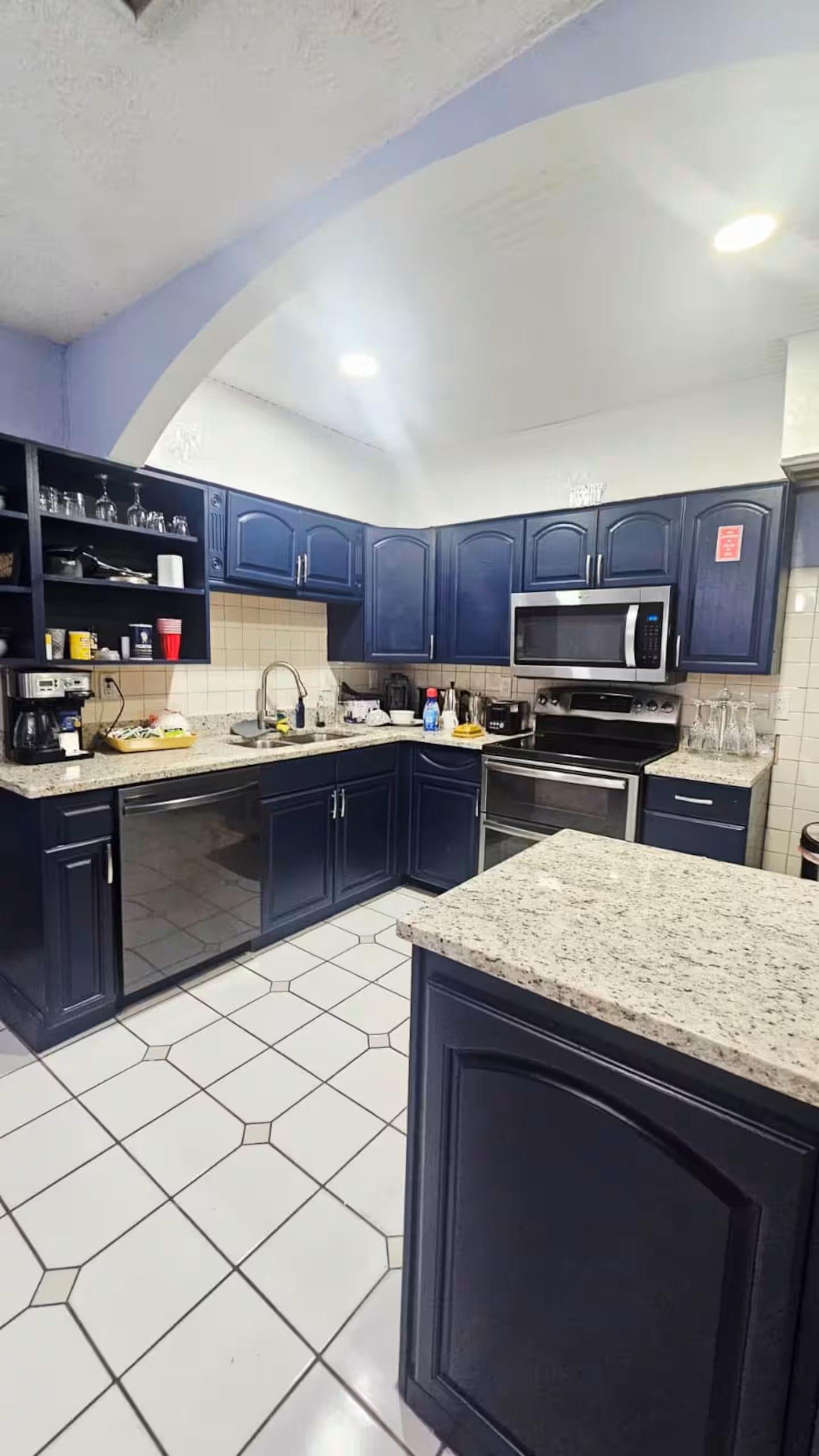 A kitchen with dark blue cabinets, a microwave, a stove, and a tiled floor.