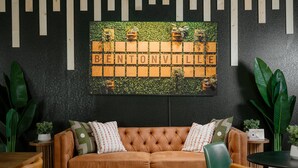 A cozy room with a brown leather sofa, green and patterned cushions, a wooden wall art piece spelling 'BENTONVILLE,' and large green plants. - Independent Boutique Hotel Suite Near Bentonville's Top Sights (Bentonville)