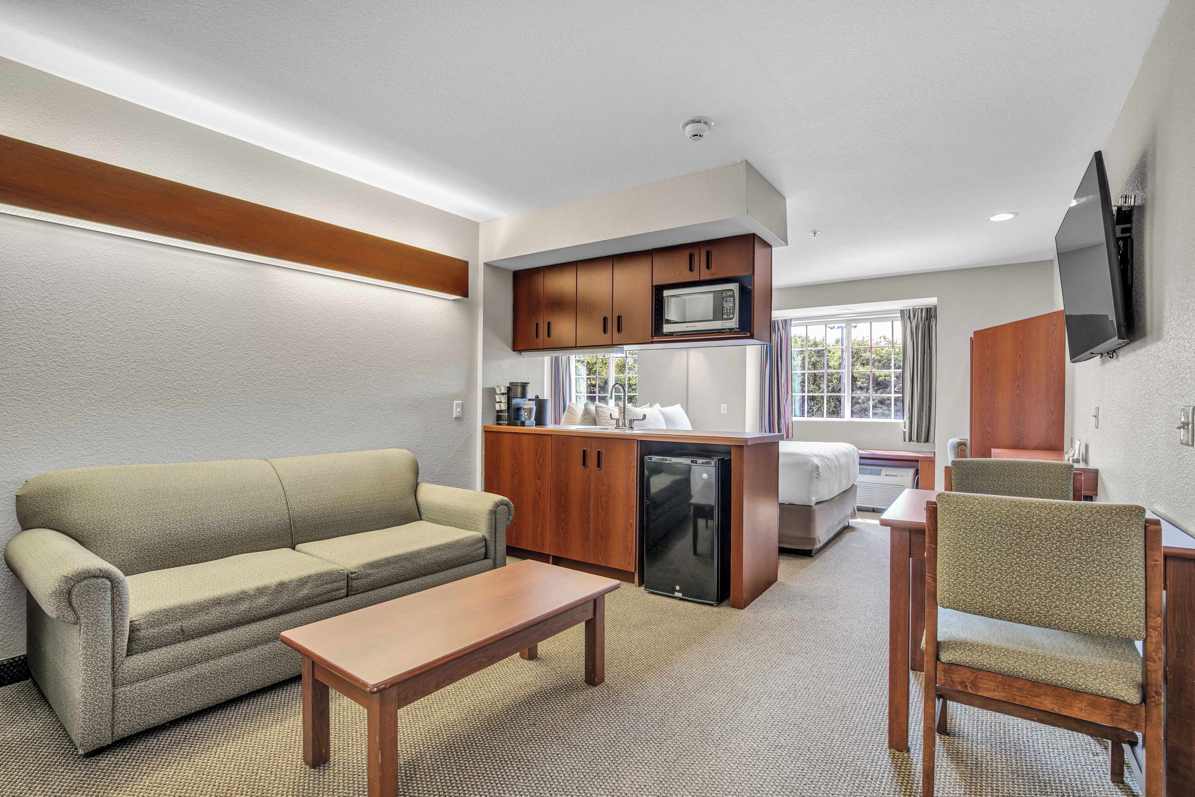 Habitación de hotel compacta con kitchenette, un sofá, una mesa de comedor y un televisor montado en la pared.