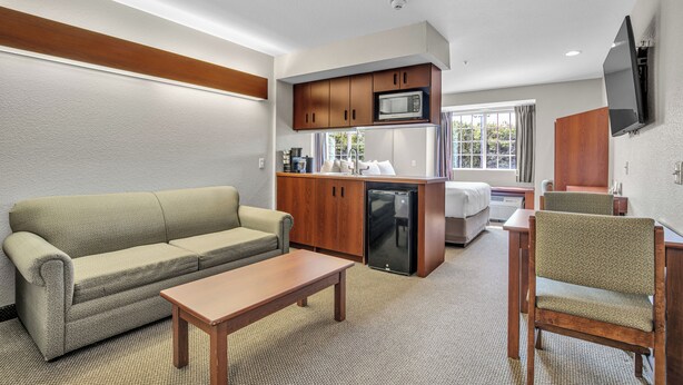 A compact hotel room with a kitchenette, a sofa, a dining table, and a TV mounted on the wall. - Independent Boutique Hotel Suite Near Bentonville's Top Sights (Bentonville)