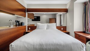 A hotel room with a large bed, wooden headboard, a flat-screen TV, a bedside table with a lamp, and a window with curtains. - Independent Boutique Hotel Suite Near Bentonville's Top Sights (Bentonville)