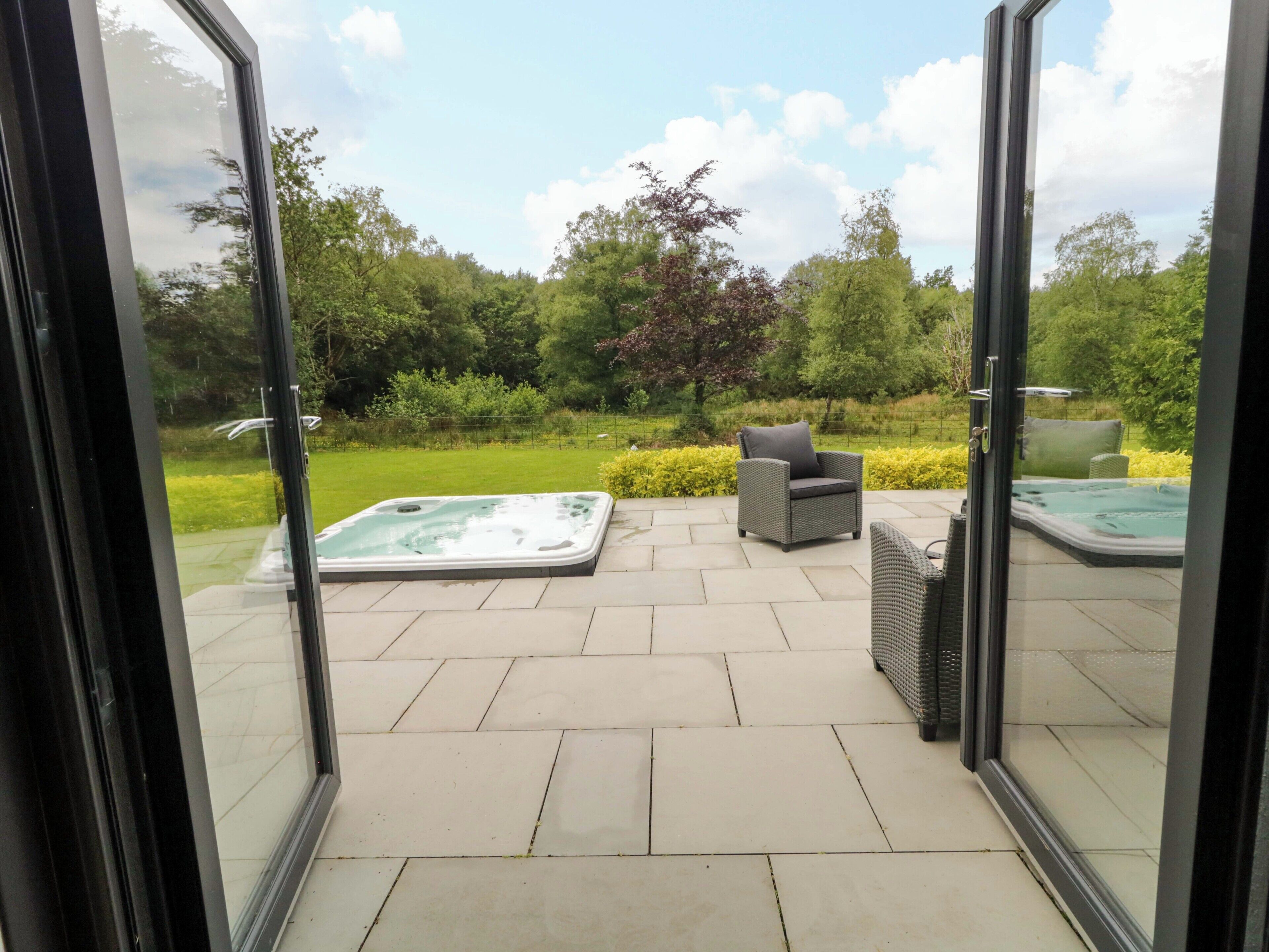 A patio area with a hot tub, outdoor seating, and a view of the garden.