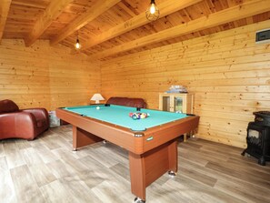 Una mesa de billar en una habitación de madera con un sofá y un armario.