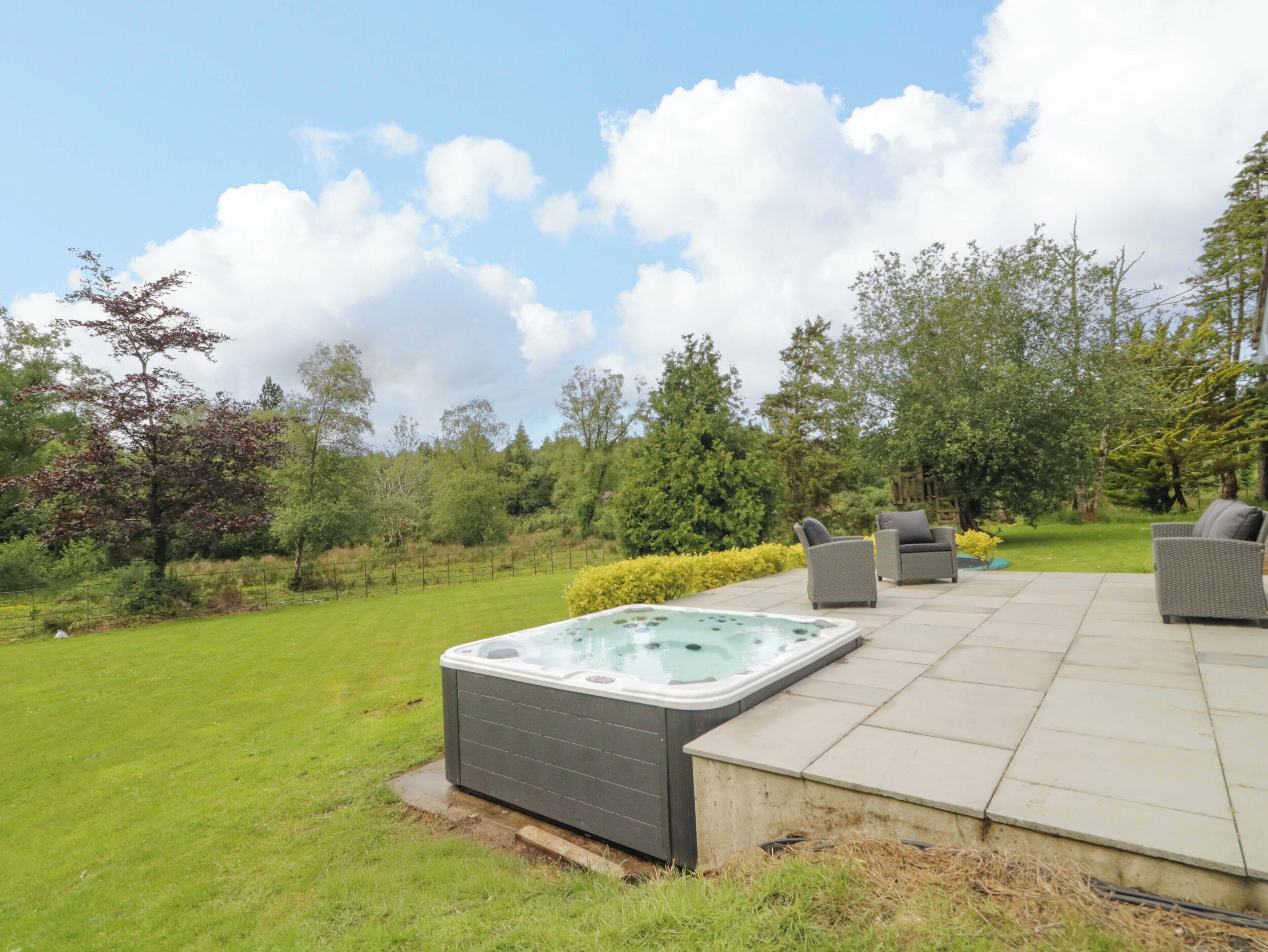 A hot tub on a patio with outdoor furniture and a grassy area.