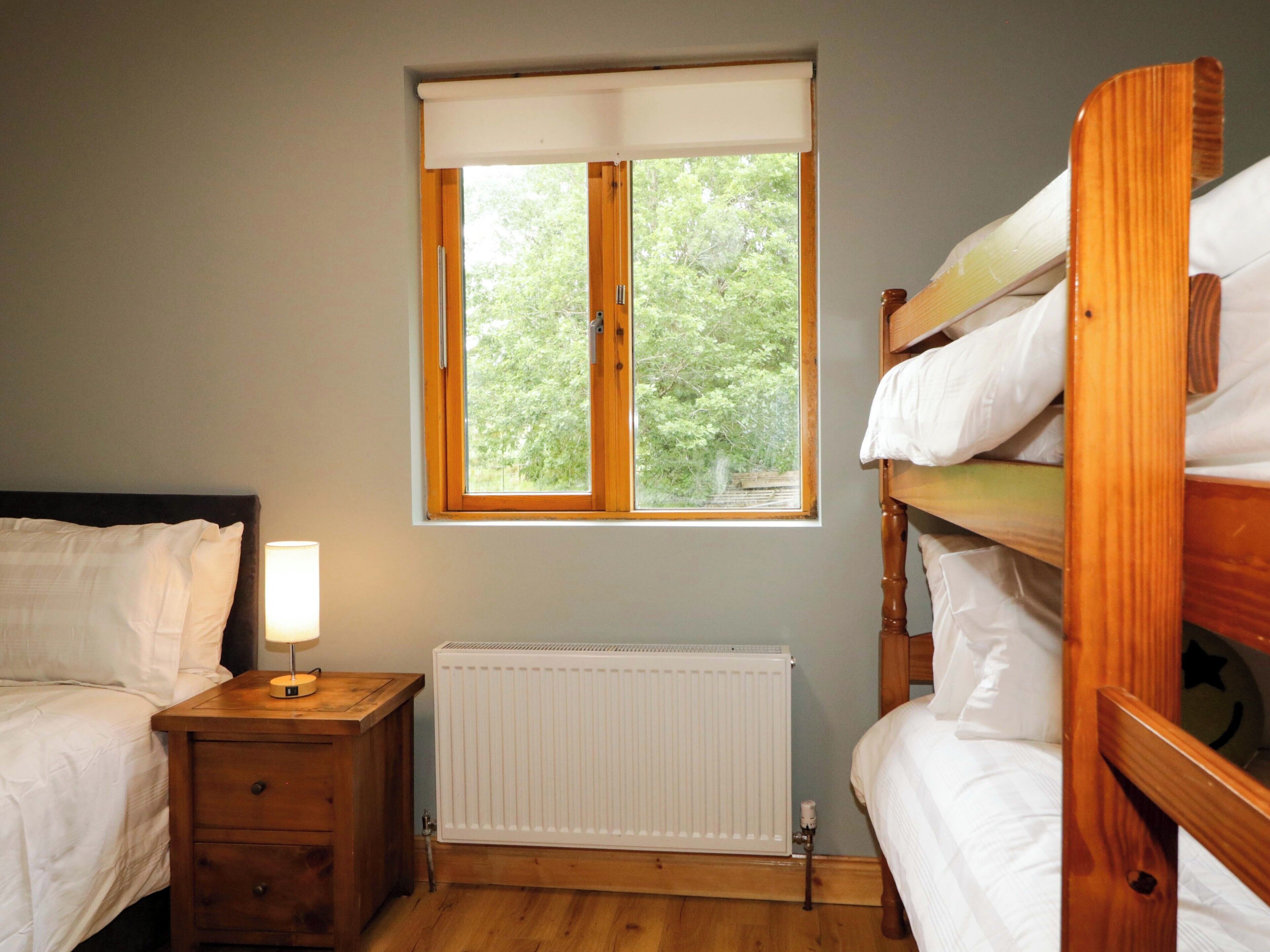 A room with a bed, a nightstand with a lamp, a radiator, and a window with a view of trees.