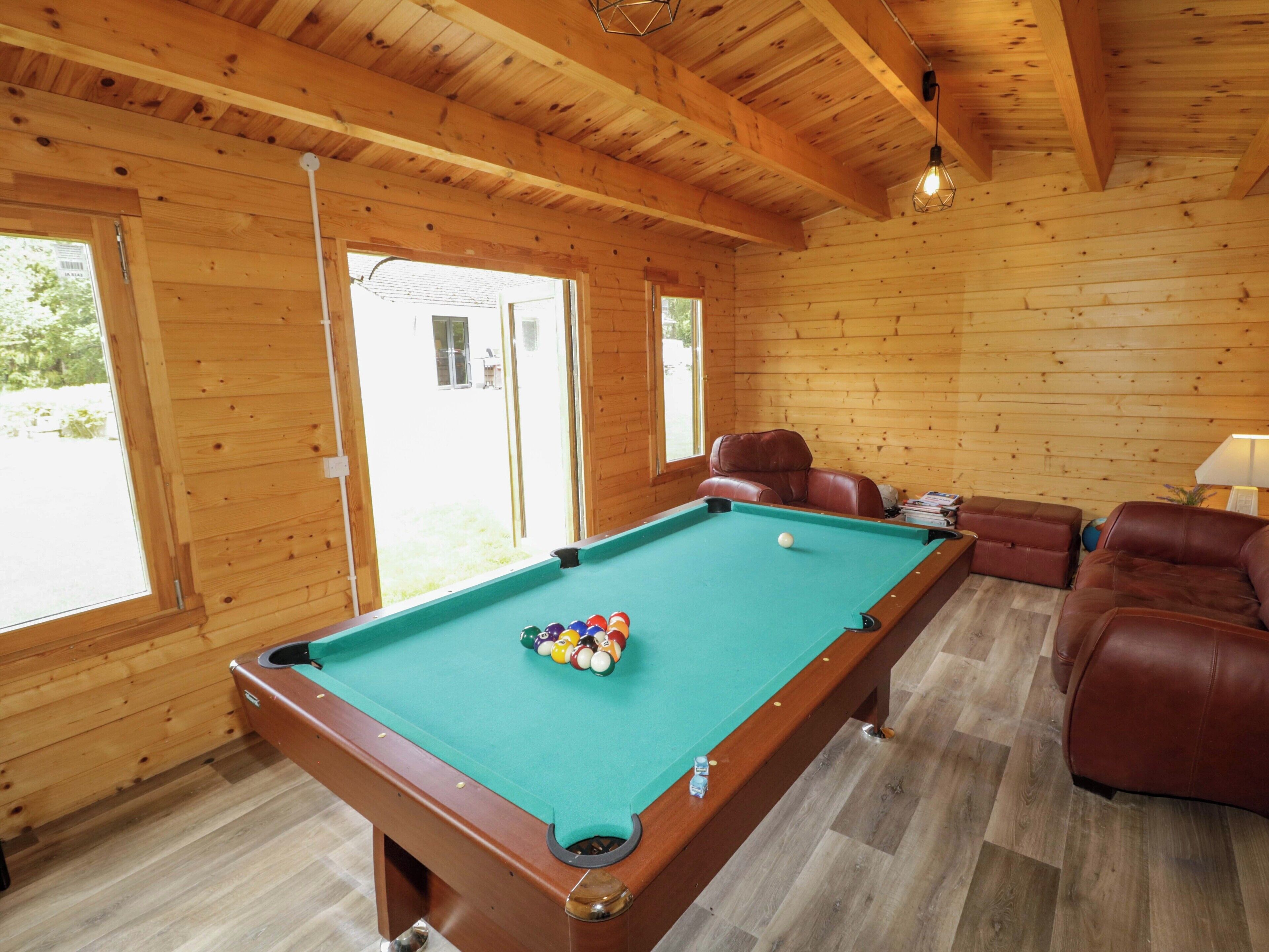A pool table with balls, a brown leather sofa, and a wooden ceiling.