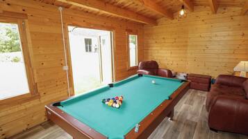 A pool table with balls, a brown leather sofa, and a wooden ceiling.