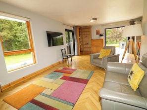 A living room with a sofa, a television, a bookshelf, and a window with a view of greenery.