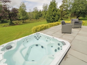 Un jacuzzi en un patio con césped y árboles al fondo.
