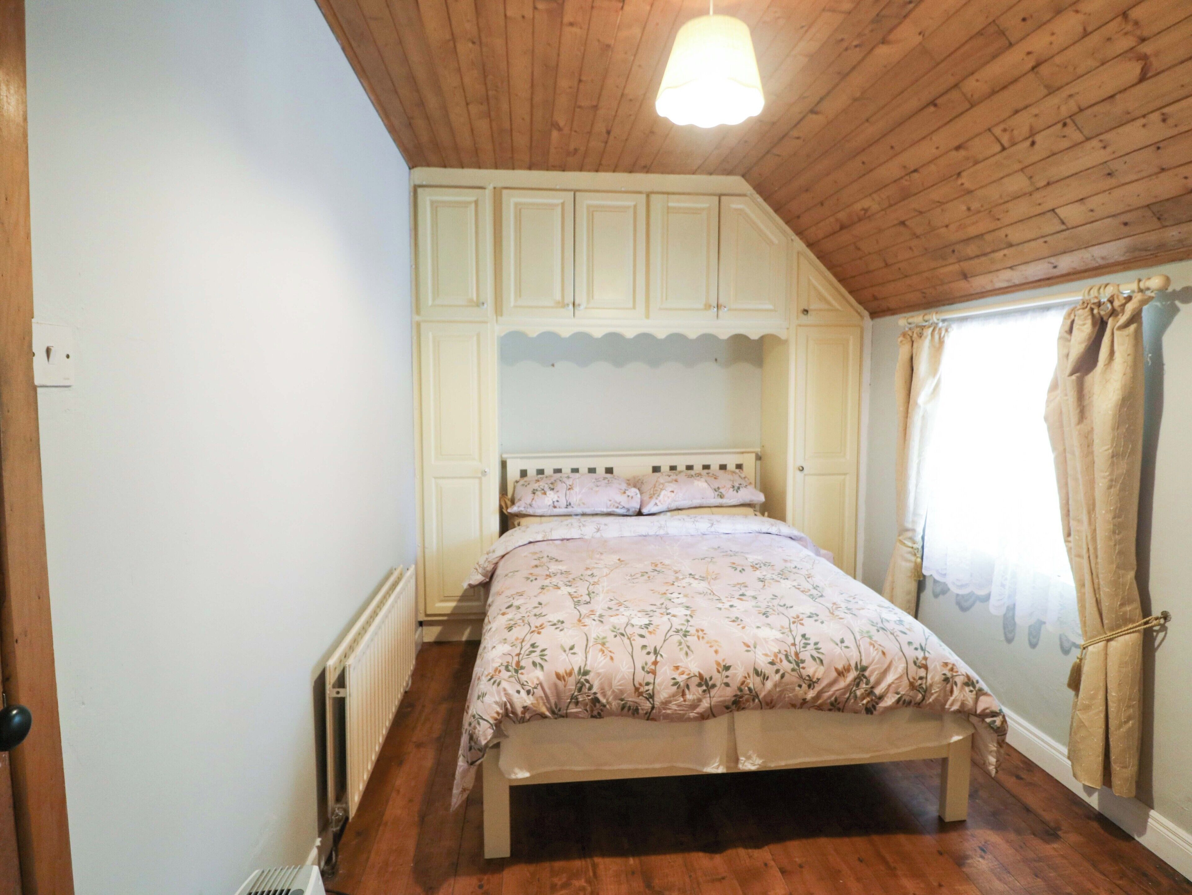 A bedroom with a wooden ceiling, a bed with floral bedding, and a window with curtains.