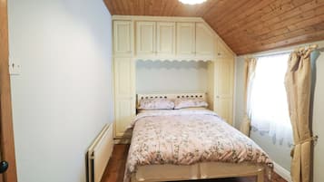 Une chambre avec un plafond en bois, un lit recouvert d’une literie à motifs floraux et une fenêtre avec des rideaux.