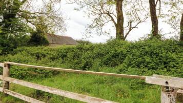 A rustic wooden fence, a hedge, and a building with a thatched roof in the background.
