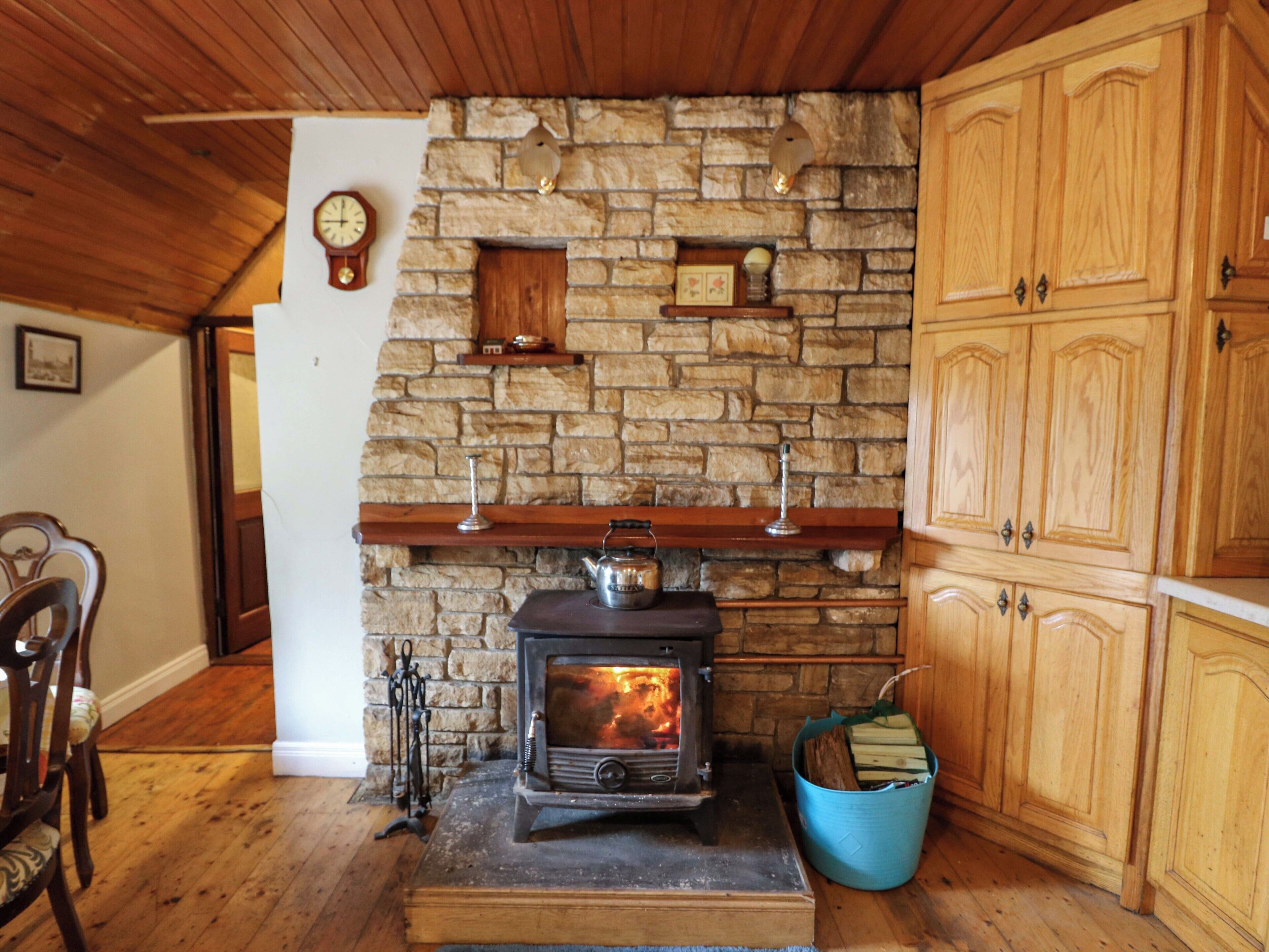 A rustic interior with a stone fireplace, wooden cabinets, and a clock on the wall.