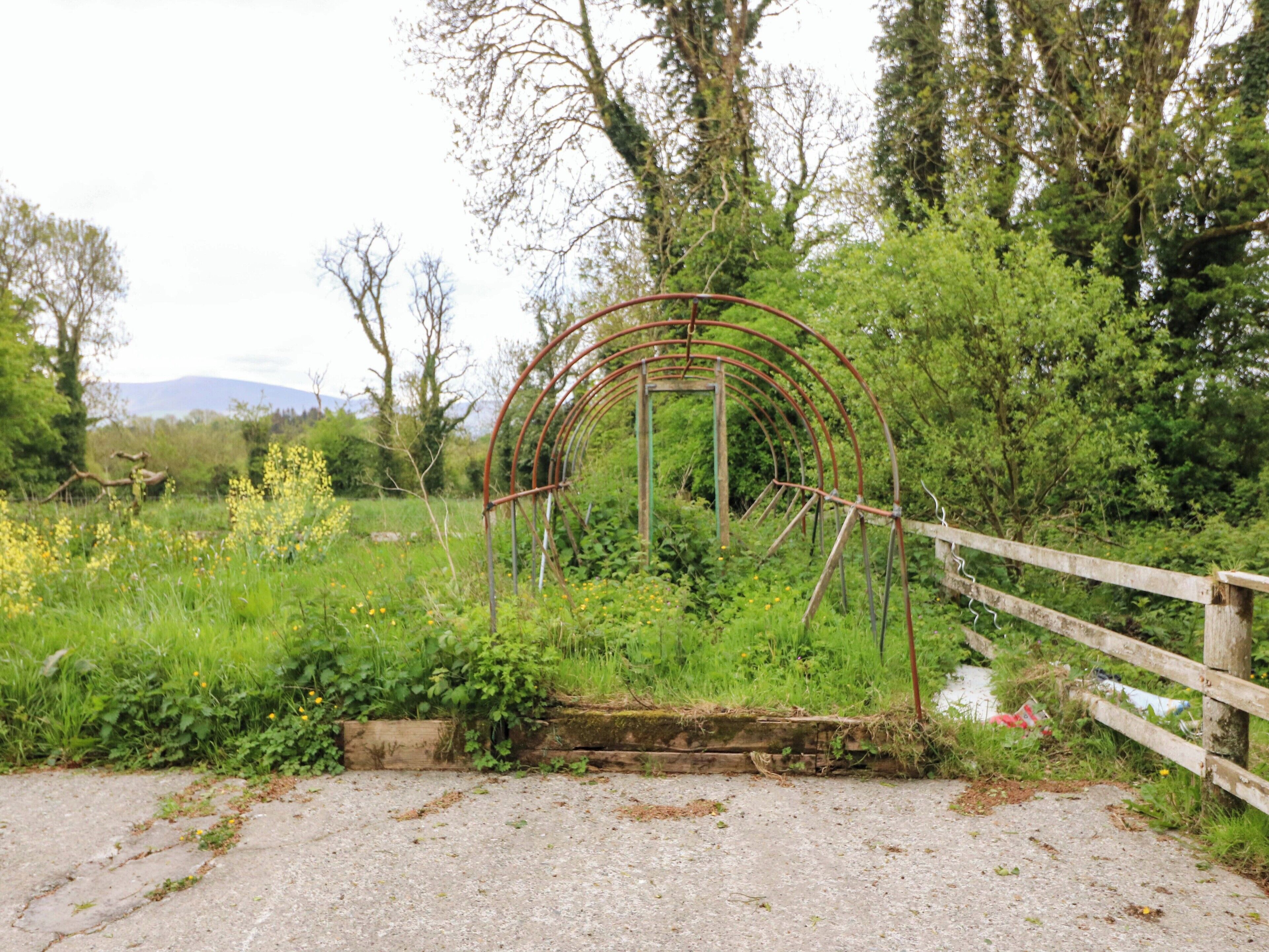 Un paysage rural avec une structure en arc métallique, une clôture en bois et un chemin de gravier.