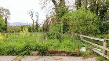 Un paysage rural avec une structure en arc métallique, une clôture en bois et un chemin de gravier.