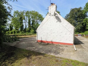 Een klein, wit gebouw met een rode basis, omgeven door groen en bomen.