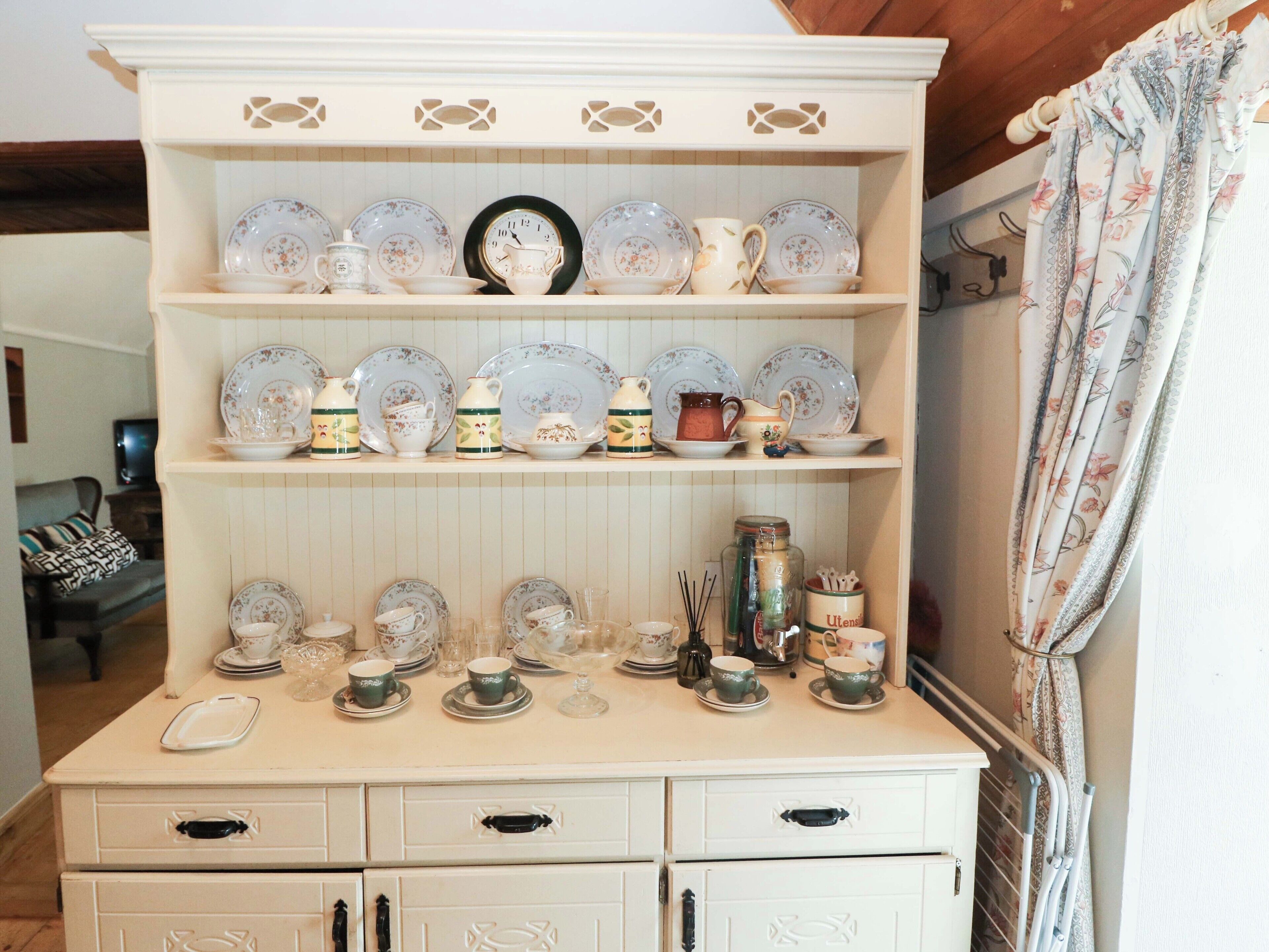 A kitchen with a white cabinet displaying various dishes and utensils.