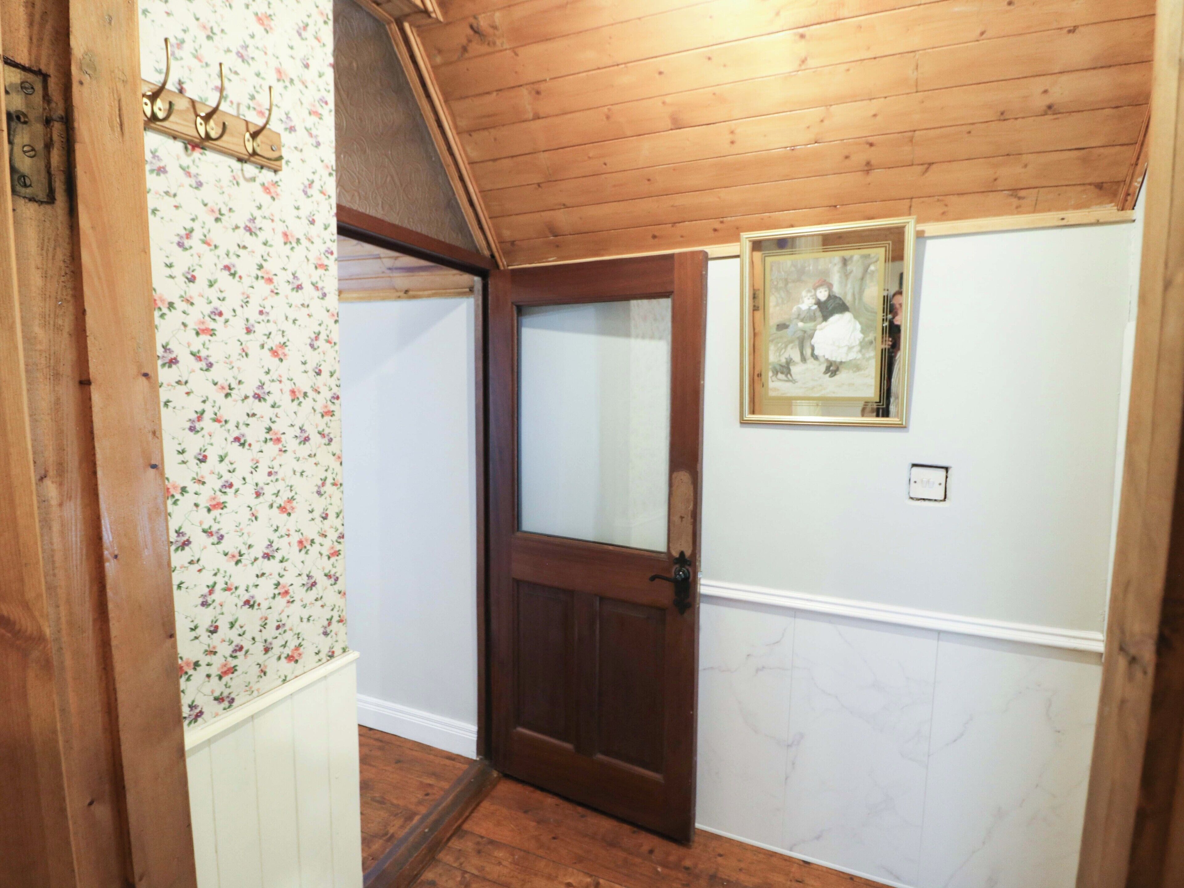 A wooden interior with a door, floral wallpaper, and a framed picture on the wall.