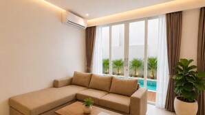 Ein modernes Wohnzimmer mit einem Ecksofa, einem Couchtisch, einer Topfpflanze und Blick auf einen Swimmingpool durch große Fenster.