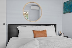 A bed with white bedding and a brown pillow, a round mirror on the wall, and a blue abstract painting. - Suburban Escape - Close to Perth CBD (Yokine)