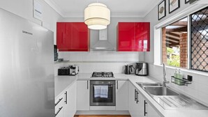 Una cocina moderna con armarios blancos, detalles en rojo, electrodomésticos de acero inoxidable y un ventanal grande.
