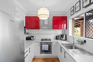 A modern kitchen with white cabinets, red accents, stainless steel appliances, and a large window. - Suburban Escape - Close to Perth CBD (Yokine)