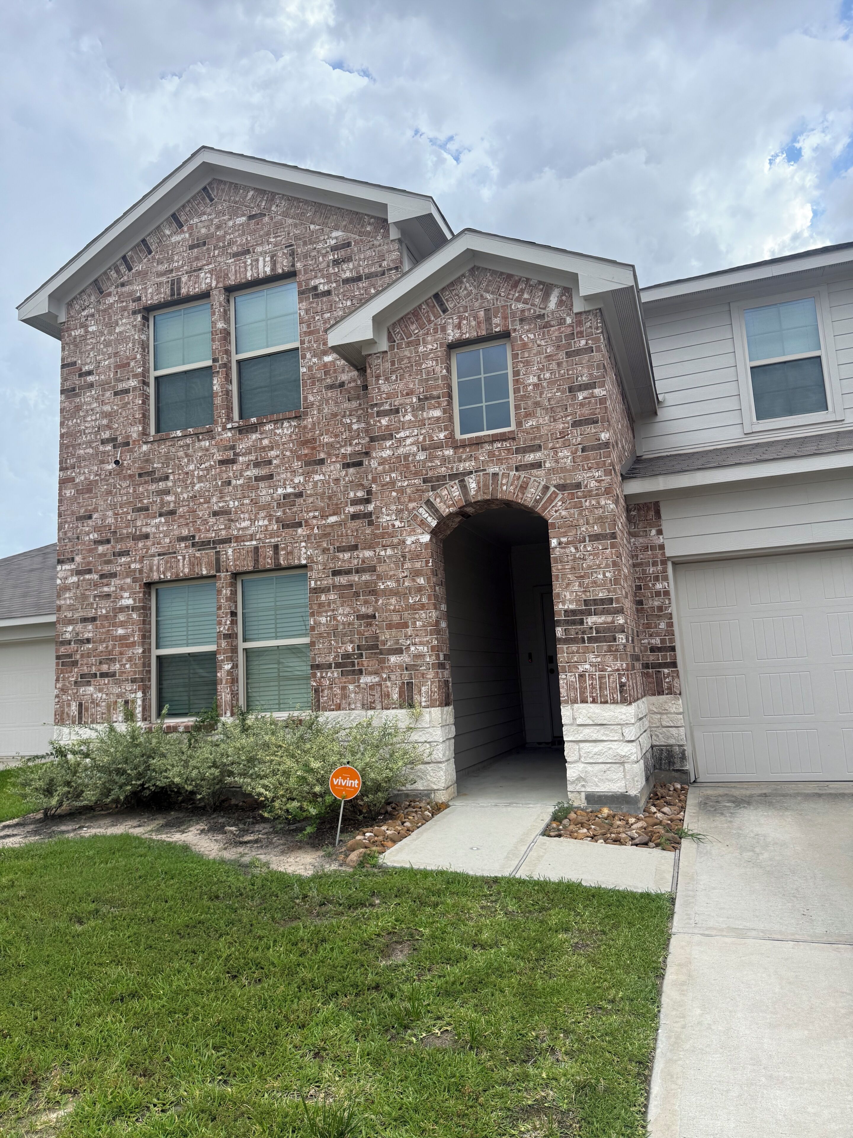 A two-story brick house with a garage, a driveway, and a well-maintained lawn.