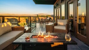 Une terrasse sur le toit dotée d’un foyer, de meubles en osier et d’un espace repas fermé par des parois de verre.